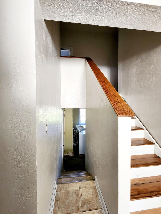 stairway featuring baseboards, a textured wall, and stone finish flooring