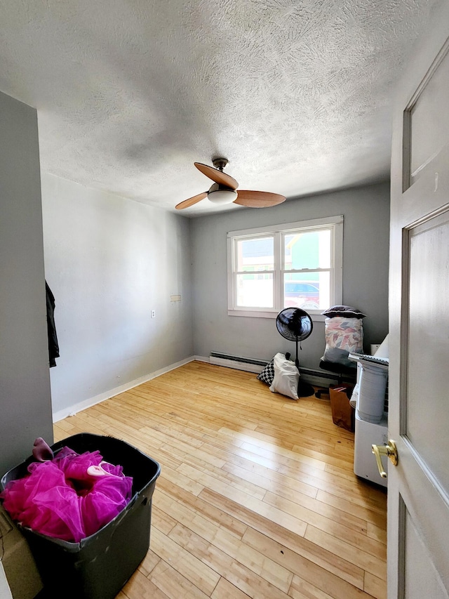 interior space featuring a textured ceiling, wood finished floors, ceiling fan, and a baseboard heating unit