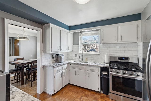 kitchen featuring stainless steel gas range, a sink, white cabinetry, and light stone countertops