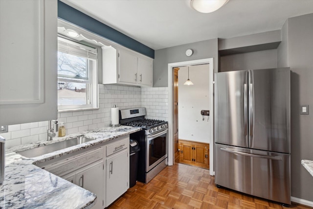 kitchen featuring white cabinets, light stone counters, a sink, stainless steel appliances, and decorative backsplash
