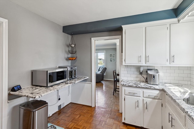 kitchen with light stone countertops, tasteful backsplash, stainless steel microwave, and white cabinets