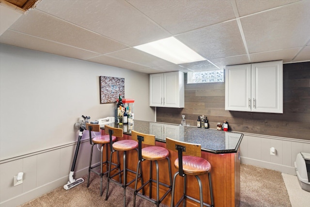 bar featuring a bar, wainscoting, carpet flooring, and a drop ceiling