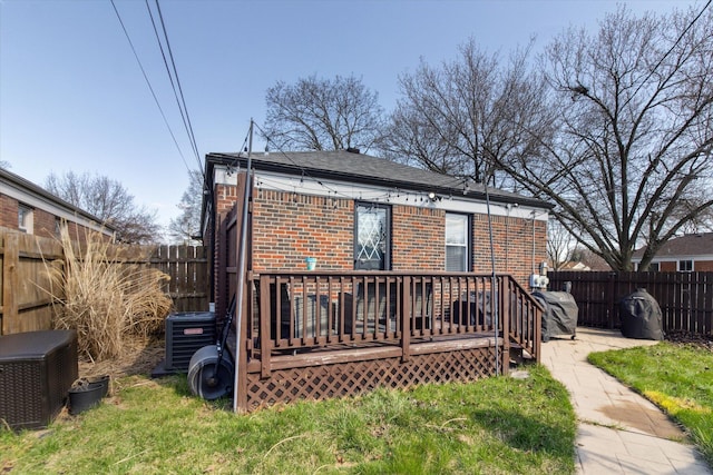 rear view of house with central air condition unit, brick siding, a fenced backyard, and a wooden deck