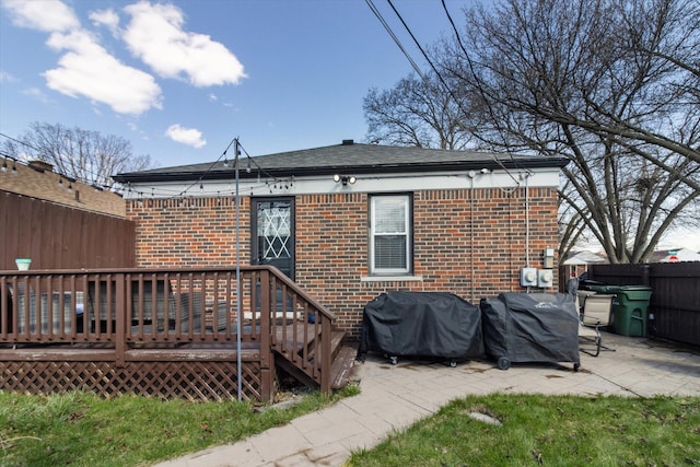 rear view of property with a deck, a patio area, fence, brick siding, and roof with shingles