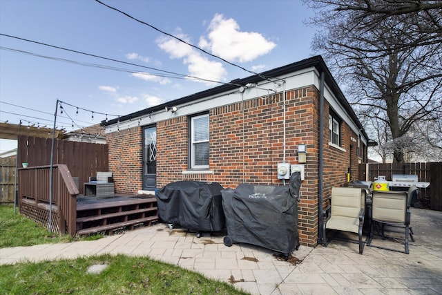 rear view of property featuring a patio, brick siding, a deck, and fence