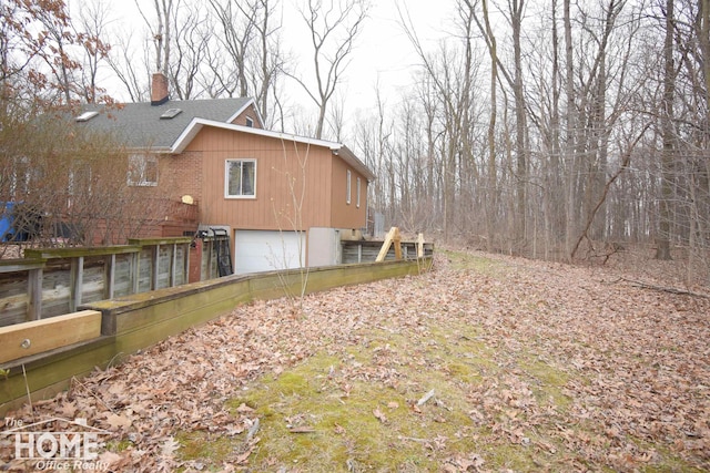 view of side of home with an attached garage, a shingled roof, and a chimney