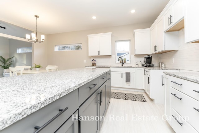 kitchen featuring a notable chandelier, a sink, light stone countertops, gray cabinets, and backsplash
