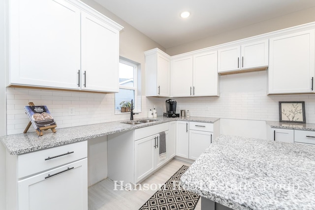 kitchen featuring white cabinetry, recessed lighting, light stone counters, a sink, and decorative backsplash