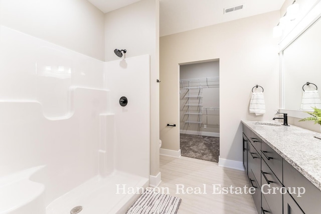 bathroom featuring vanity, baseboards, a spacious closet, a walk in shower, and visible vents