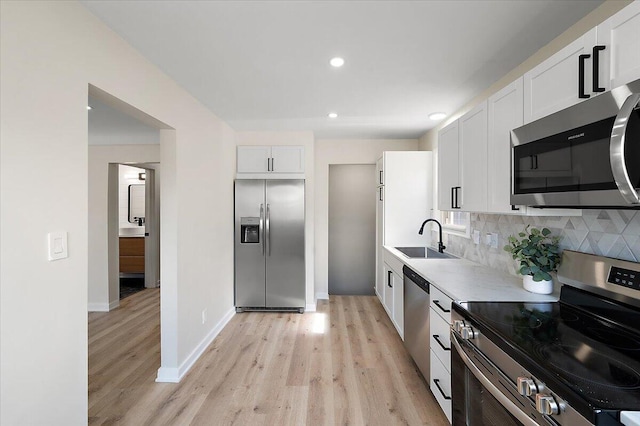 kitchen with light wood-type flooring, backsplash, white cabinets, appliances with stainless steel finishes, and a sink