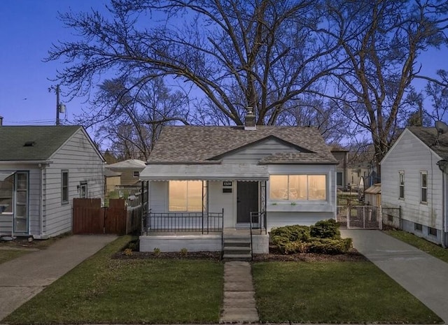 bungalow-style house with a gate, a front yard, fence, a shingled roof, and covered porch