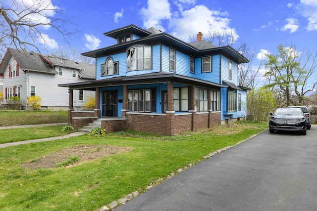 view of front of house featuring a chimney, brick siding, a front yard, and covered porch