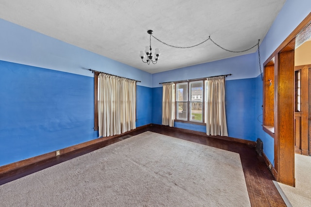empty room featuring visible vents, baseboards, an inviting chandelier, and dark wood-style floors