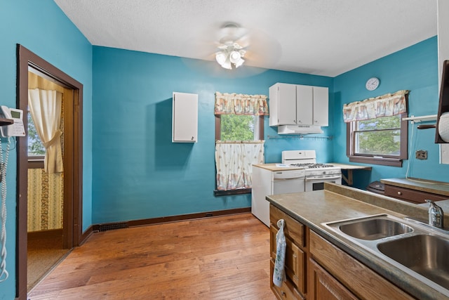 kitchen with white cabinets, under cabinet range hood, white range with gas stovetop, a sink, and light wood-style floors
