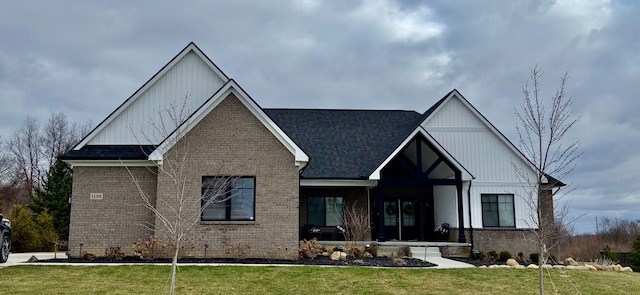view of front of home featuring brick siding, a front lawn, and roof with shingles
