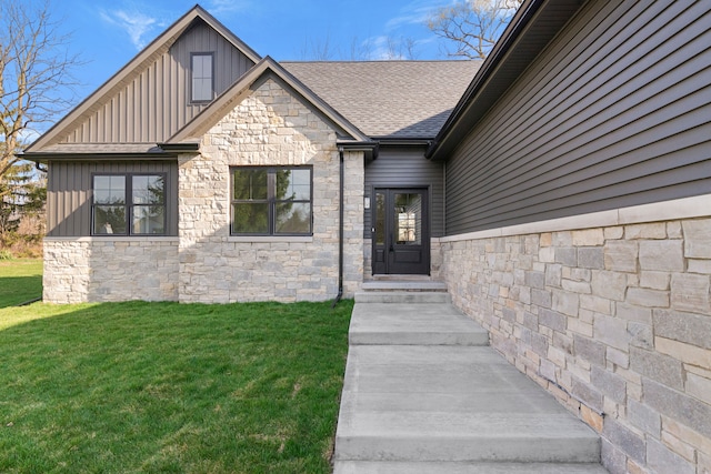 view of exterior entry with roof with shingles, board and batten siding, stone siding, and a yard