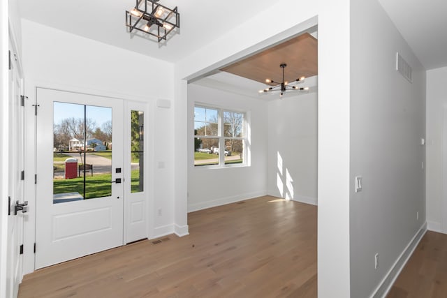 entryway featuring baseboards, a notable chandelier, wood finished floors, and visible vents