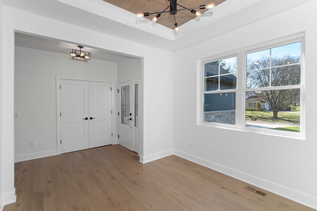 unfurnished room with baseboards, a notable chandelier, wood finished floors, and visible vents