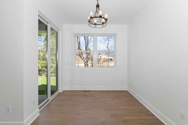 unfurnished dining area with wood finished floors, baseboards, and a notable chandelier