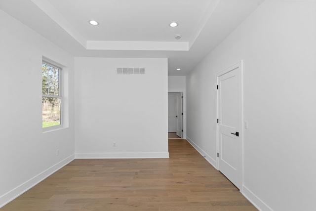 unfurnished bedroom with a tray ceiling, light wood finished floors, baseboards, visible vents, and recessed lighting