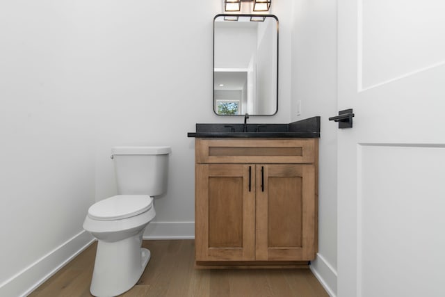 half bath with vanity, baseboards, toilet, and wood finished floors
