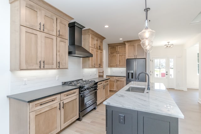 kitchen featuring wall chimney exhaust hood, light brown cabinetry, stainless steel fridge, and high end black range oven
