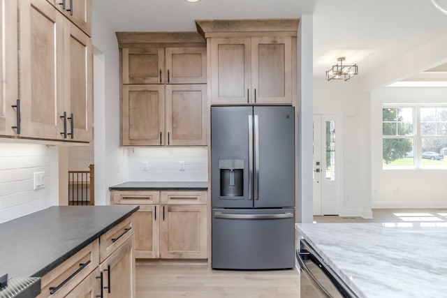 kitchen with dark stone countertops, an inviting chandelier, decorative backsplash, light brown cabinets, and appliances with stainless steel finishes