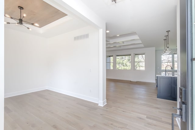 interior space with light wood-style flooring, baseboards, a notable chandelier, visible vents, and a raised ceiling