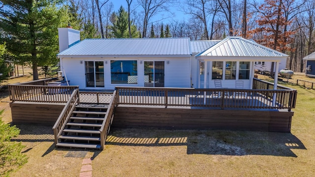 back of house with a deck, metal roof, stairs, and a chimney