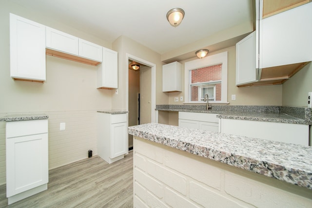 kitchen with light wood-type flooring, white cabinetry, a wainscoted wall, light stone counters, and a sink