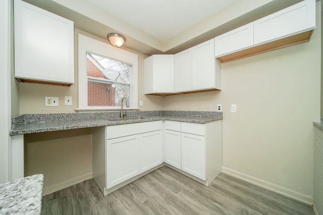 kitchen with light stone countertops, light wood finished floors, a sink, and white cabinets