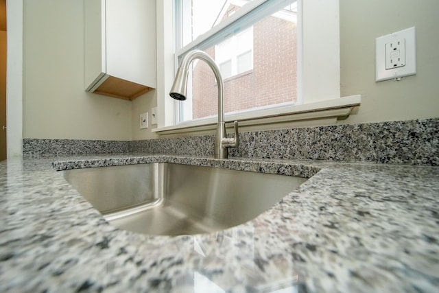 details featuring a sink, white cabinets, and light stone counters