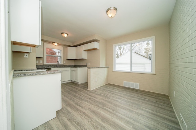 kitchen featuring white cabinets, visible vents, a sink, brick wall, and light wood finished floors