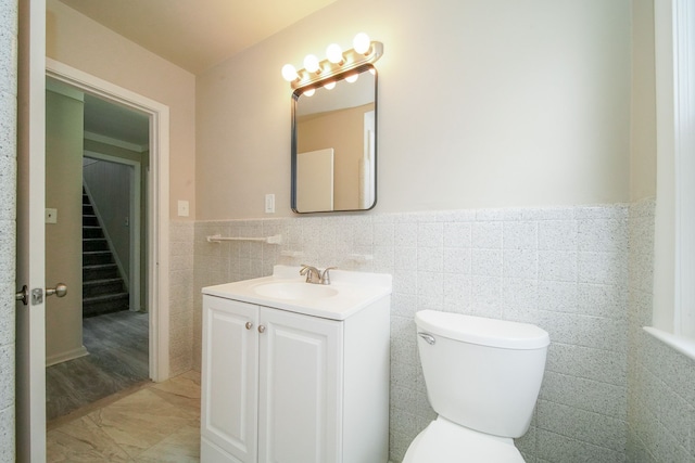 half bath featuring toilet, vanity, wainscoting, and tile walls