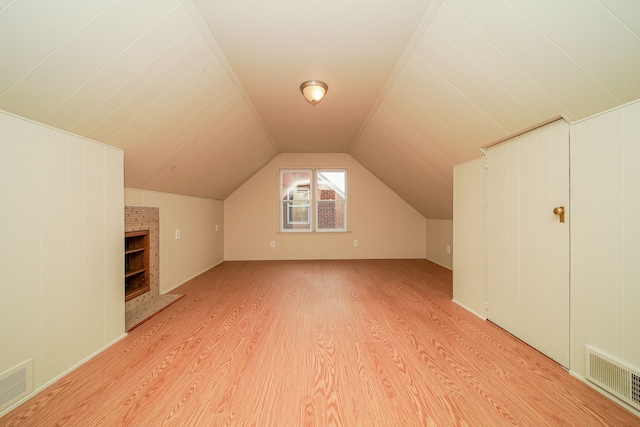 bonus room with light wood-type flooring, a fireplace, lofted ceiling, and visible vents