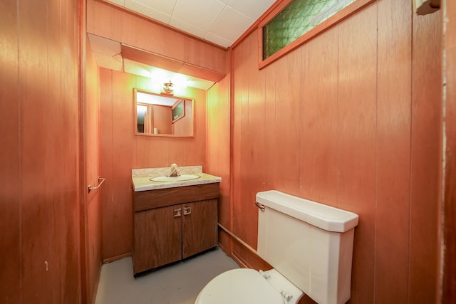 bathroom with wooden walls, vanity, toilet, and finished concrete flooring