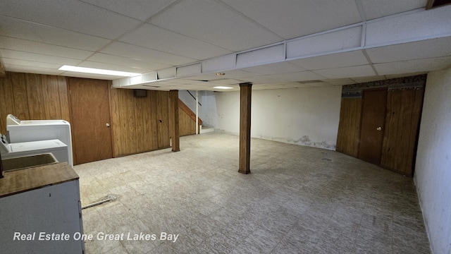 finished basement featuring wooden walls, washer / dryer, a paneled ceiling, and stairs