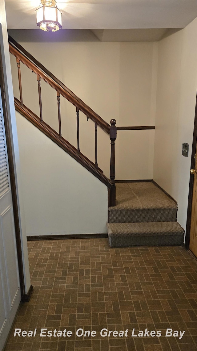 staircase with baseboards and brick patterned floor