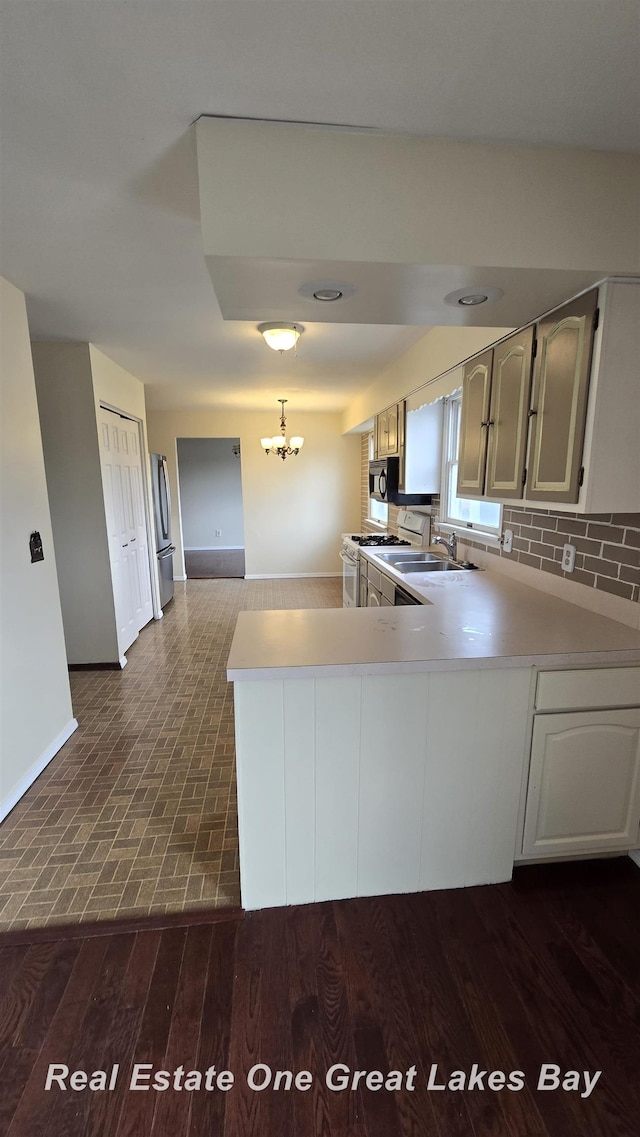kitchen featuring a notable chandelier, baseboards, light countertops, freestanding refrigerator, and a sink