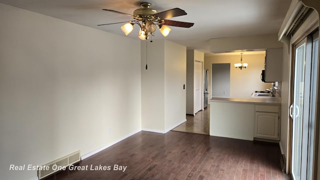interior space featuring ceiling fan with notable chandelier, a peninsula, visible vents, baseboards, and dark wood-style floors