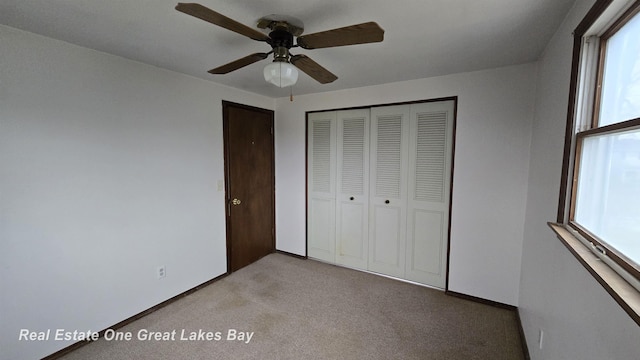 unfurnished bedroom with a closet, light colored carpet, baseboards, and a ceiling fan