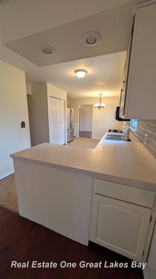 kitchen featuring a sink, light countertops, freestanding refrigerator, a peninsula, and backsplash