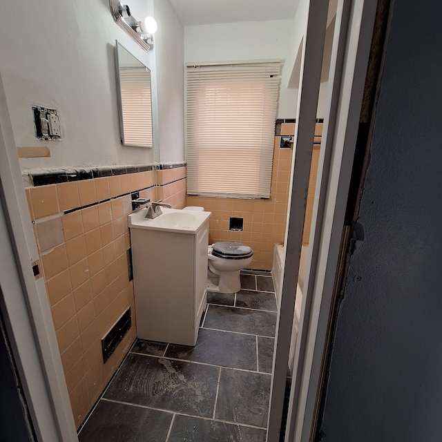 bathroom with tile walls, vanity, toilet, a wainscoted wall, and tile patterned flooring