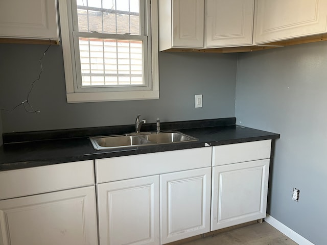 kitchen featuring a sink, dark countertops, white cabinetry, and baseboards