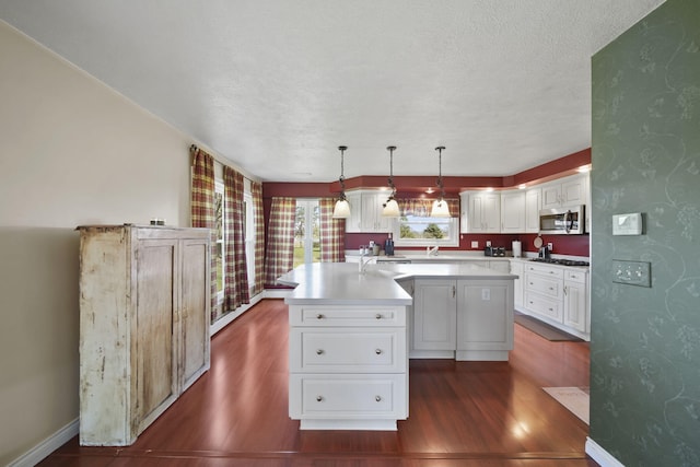 kitchen featuring wallpapered walls, stainless steel microwave, a center island, and dark wood finished floors