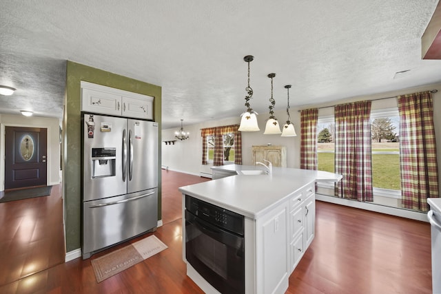kitchen featuring a textured ceiling, stainless steel refrigerator with ice dispenser, dark wood-style flooring, light countertops, and black oven