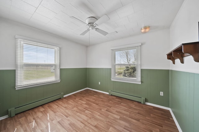 unfurnished room with a baseboard radiator, wood finished floors, ceiling fan, and a wainscoted wall