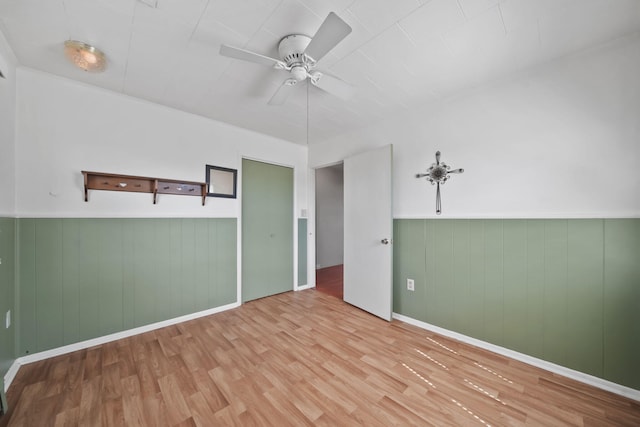 empty room featuring ceiling fan, wood finished floors, wainscoting, wooden walls, and baseboards