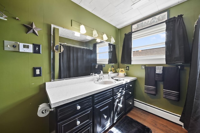 full bath with a shower with curtain, a baseboard heating unit, wood finished floors, and vanity