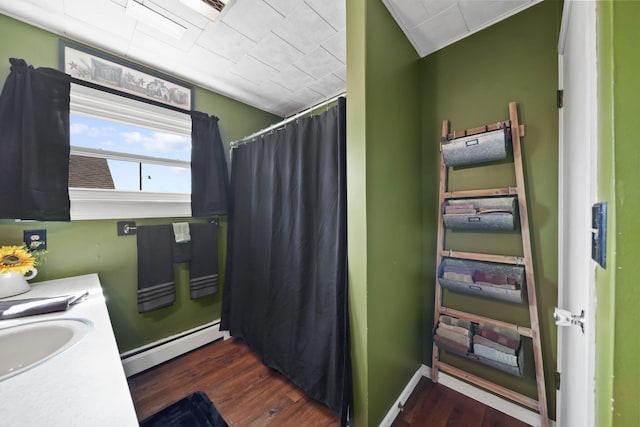 full bath featuring curtained shower, wood finished floors, a baseboard heating unit, and a sink